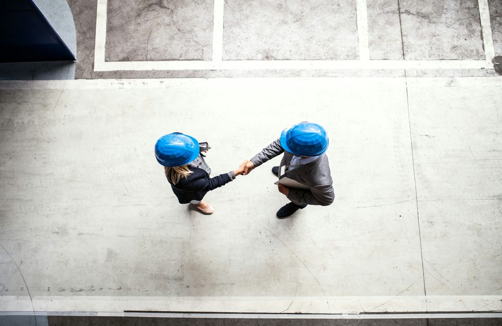Deux professionnels de la construction portant des casques de sécurité se serrent la main, illustrant les connexions créées grâce à un réseau de construction.