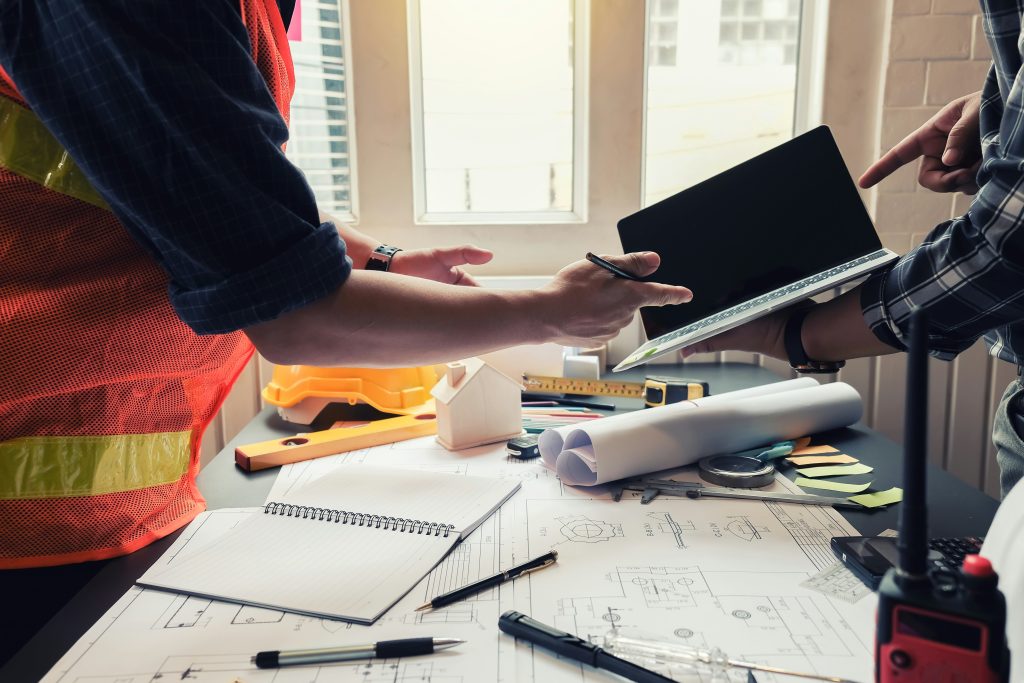 Professionnels de la construction consultant un ordinateur portable autour de plans de chantier et d’équipements de construction.